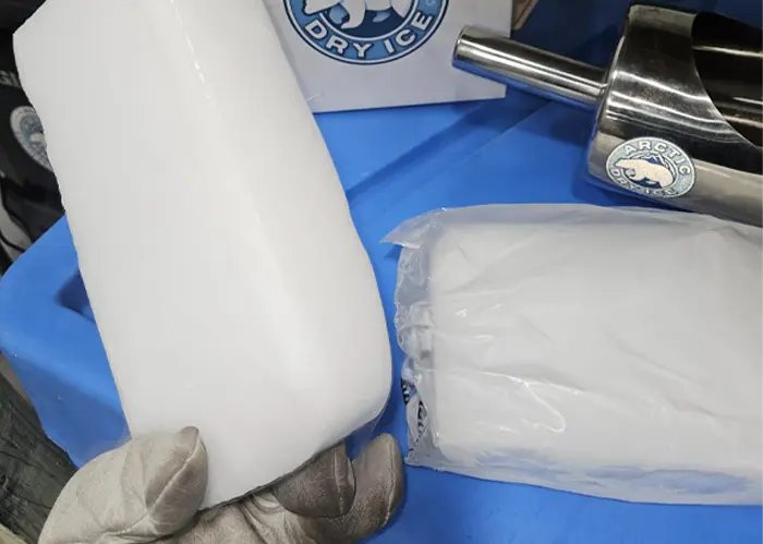 Gloved hand holding a solid dry ice block next to a bagged dry ice slice
